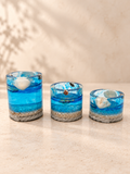 Set of three graduated ocean-blue resin candle holders with shell details on an ivory tabletop, handmade in Lancashire UK by Held Forever Studio