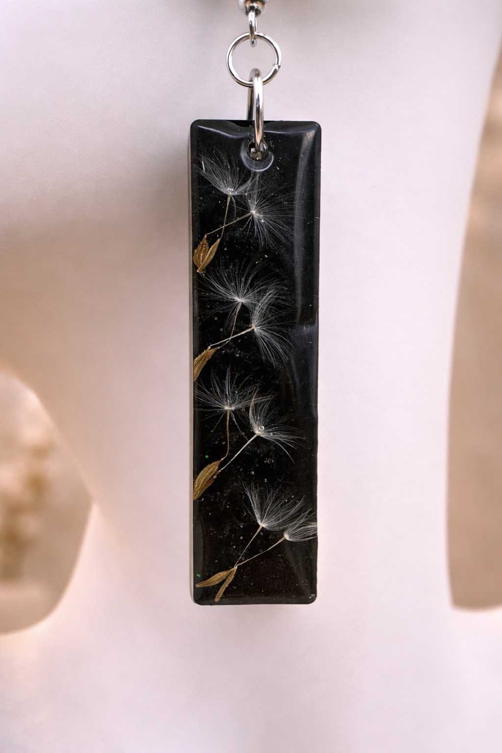 Black resin bar earring with dandelion seeds and botanical inclusions on jewellery display, handmade in Lancashire UK