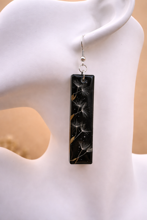 Close-up of black resin bar earring showing real dandelion seeds suspended in resin, handmade by Held Forever Studio