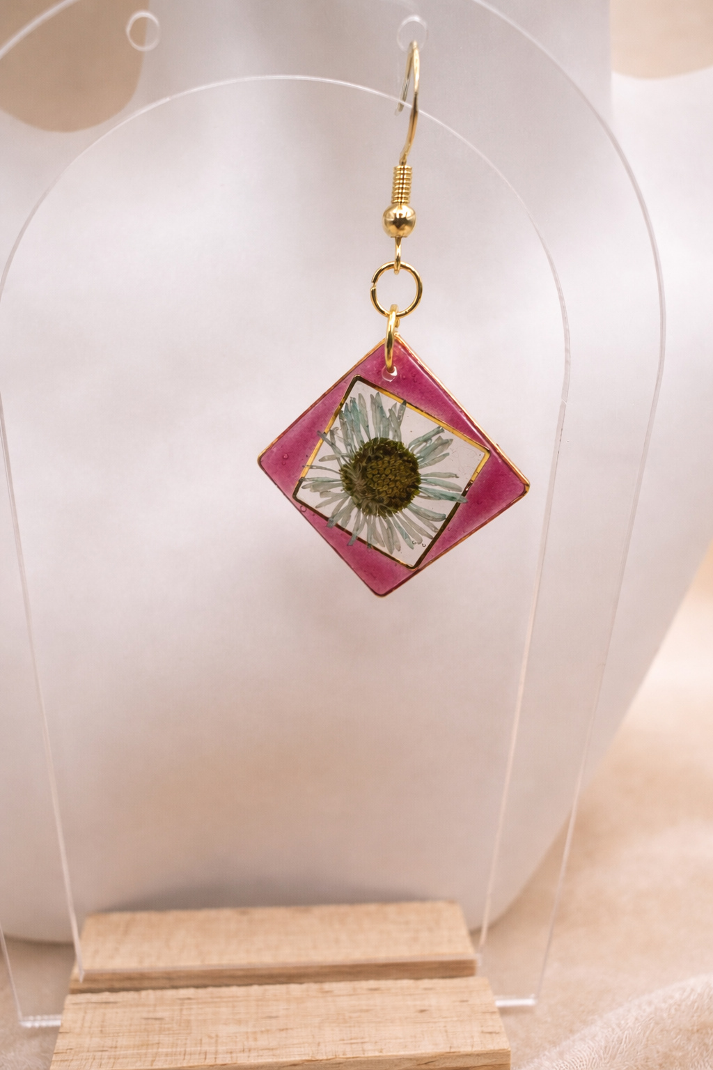 Close up of pink resin diamond drop earring with real pressed daisy worn on ear, handmade in Lancashire UK
