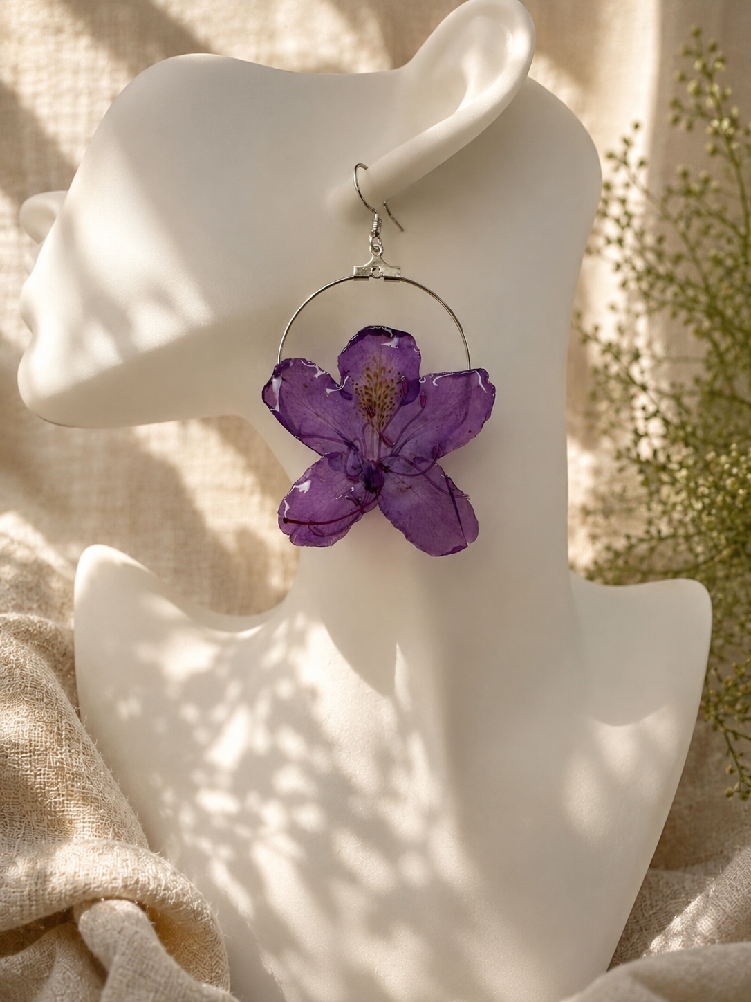 Pair of purple pressed flower resin hoop earrings with 925 sterling silver hoops on a stand, handmade in Lancashire UK
