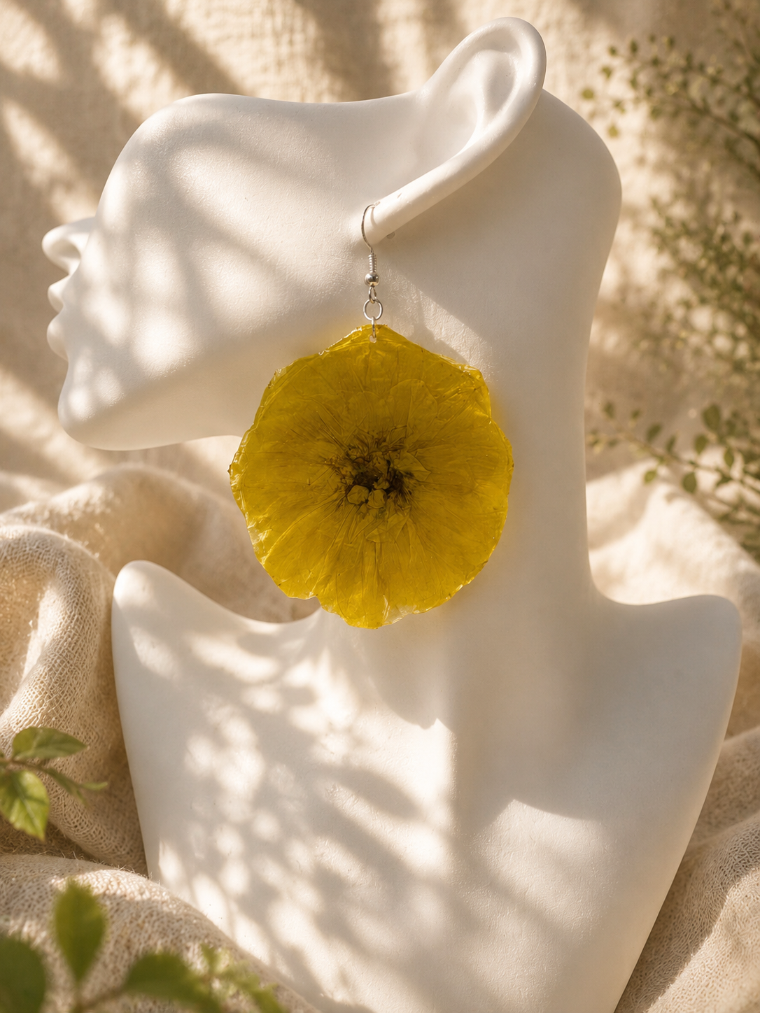 Close up of yellow pressed flower resin disc earring with 925 sterling silver hook on a display bust, handmade in Lancashire UK