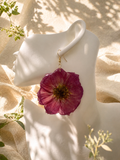 Pair of magenta pressed flower resin disc earrings with gold plated hooks on a stand, handmade by Held Forever Studio