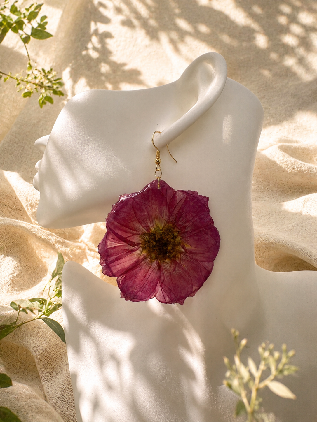 Pair of magenta pressed flower resin disc earrings with gold plated hooks on a stand, handmade by Held Forever Studio
