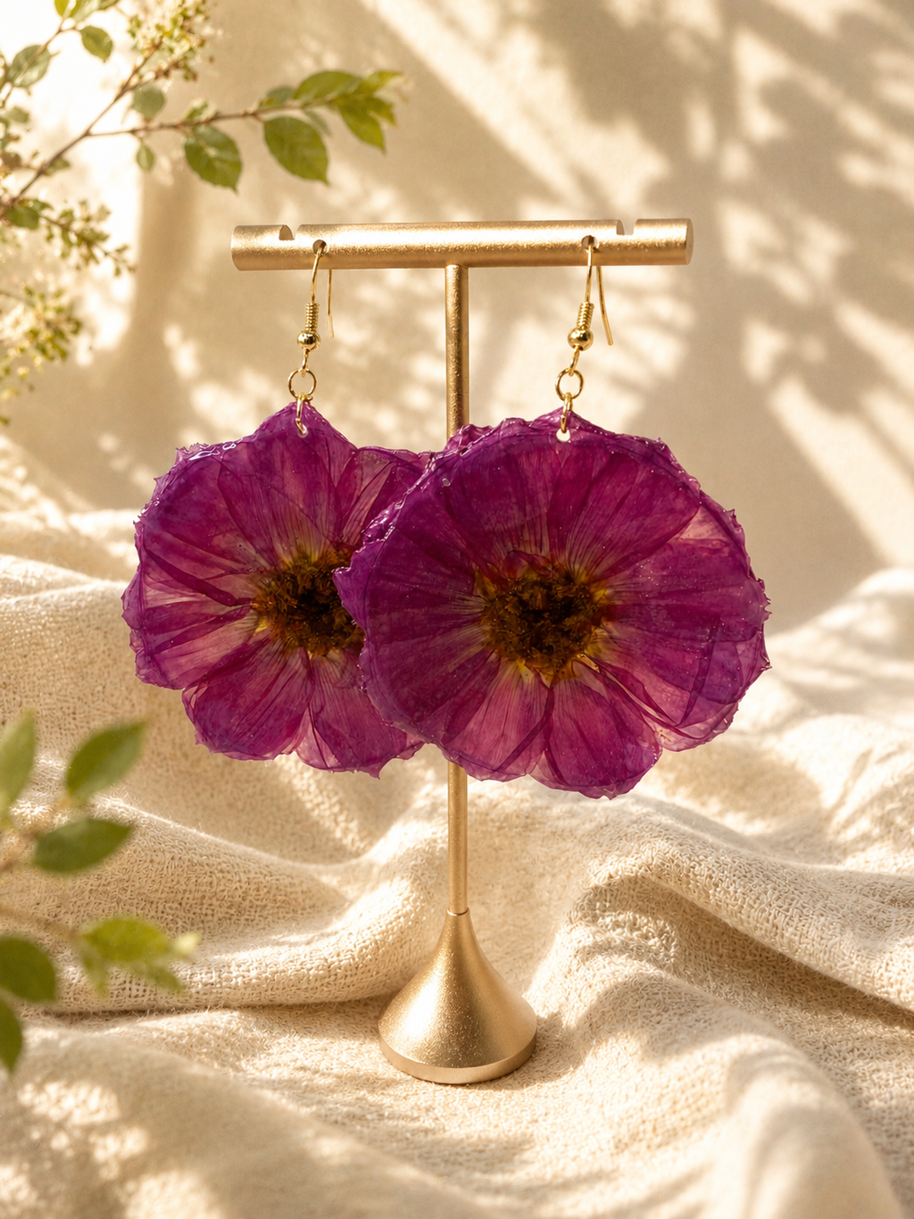 Close up of magenta pressed flower resin disc earring with gold plated hook on a display bust, handmade in Lancashire UK