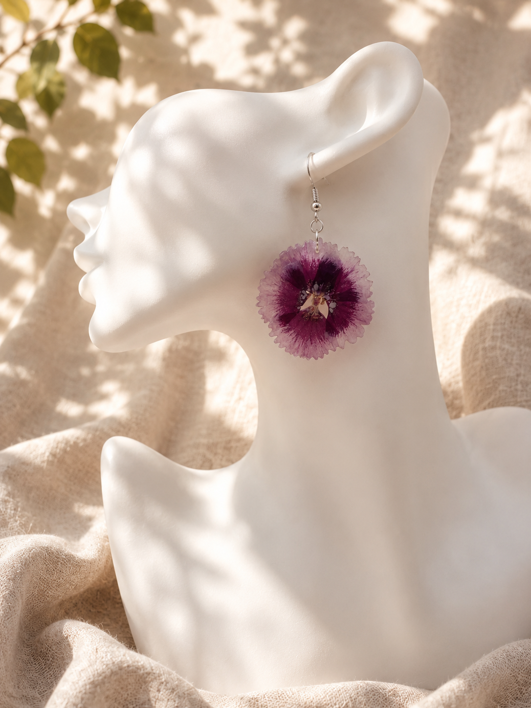 Close up of a pressed flower resin disc earring worn on the ear, showing the purple flower detail, handmade in Lancashire UK