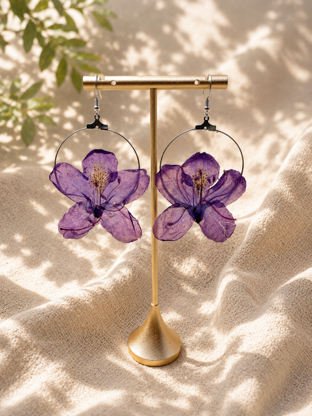 Purple pressed flower resin hoop earring with 925 sterling silver hook on a display bust, handmade by Held Forever Studio