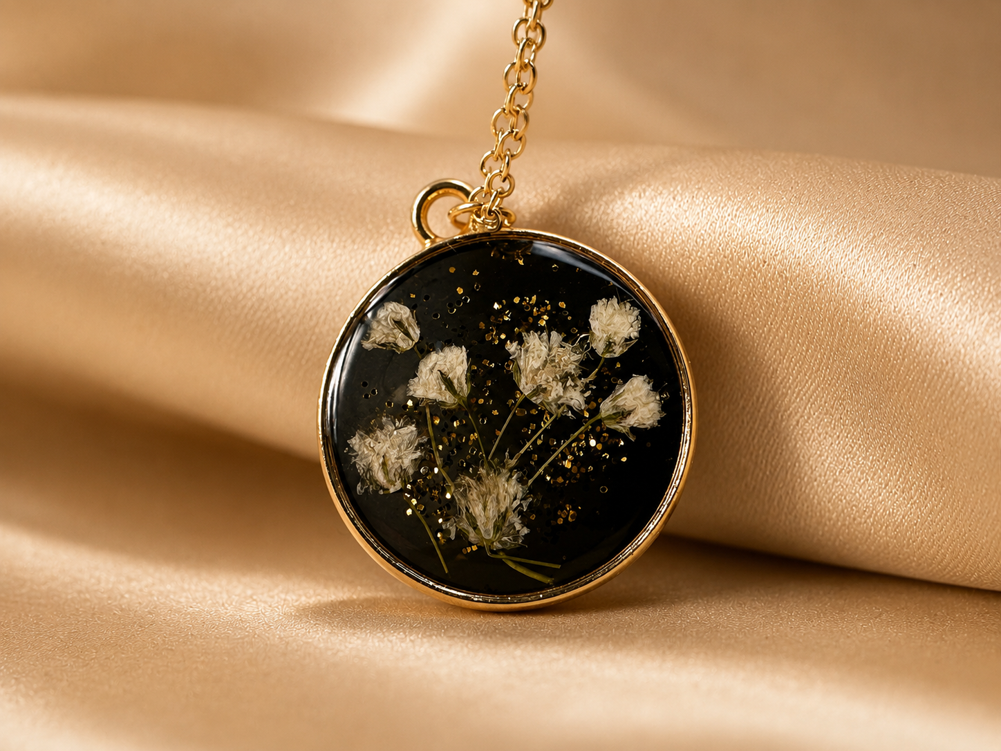 Dried flower resin pendant necklace on display stand, black resin with white flowers and gold glitter, handmade in Lancashire UK by Held Forever Studio