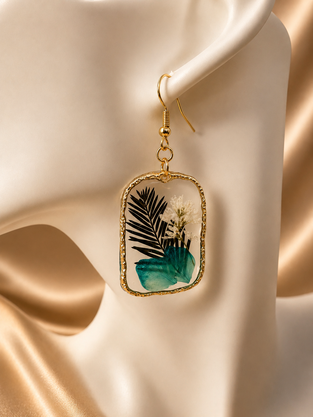 Close up of botanical resin drop earring showing dark fern fronds, teal leaf and white gypsophila in clear UV resin gold frame, handmade by Held Forever Studio