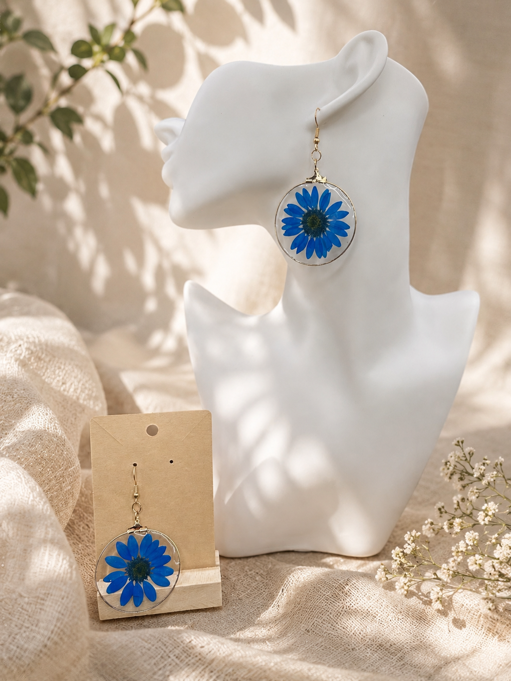 Blue daisy pressed flower resin drop earrings with gold bezel frame on display, handmade by Held Forever Studio
