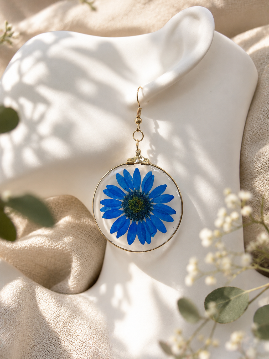Close up of clear UV resin round earring with real pressed blue daisy, handmade in Lancashire UK by Held Forever Studio