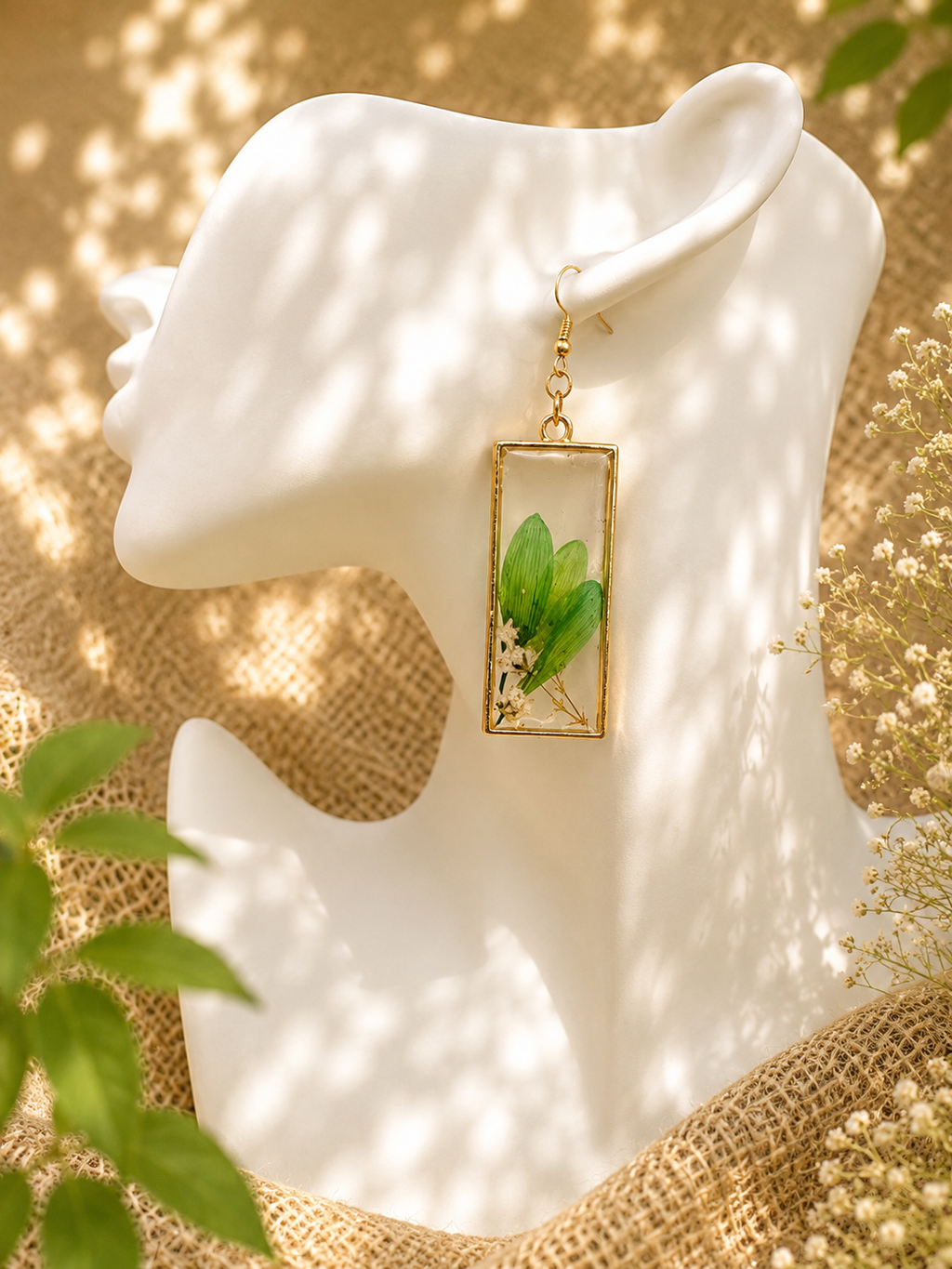 Close-up of handmade UV resin drop earrings featuring real pressed botanicals — green leaves and white flowers — in gold rectangular bezels with stainless steel hooks, by Held Forever Studio
