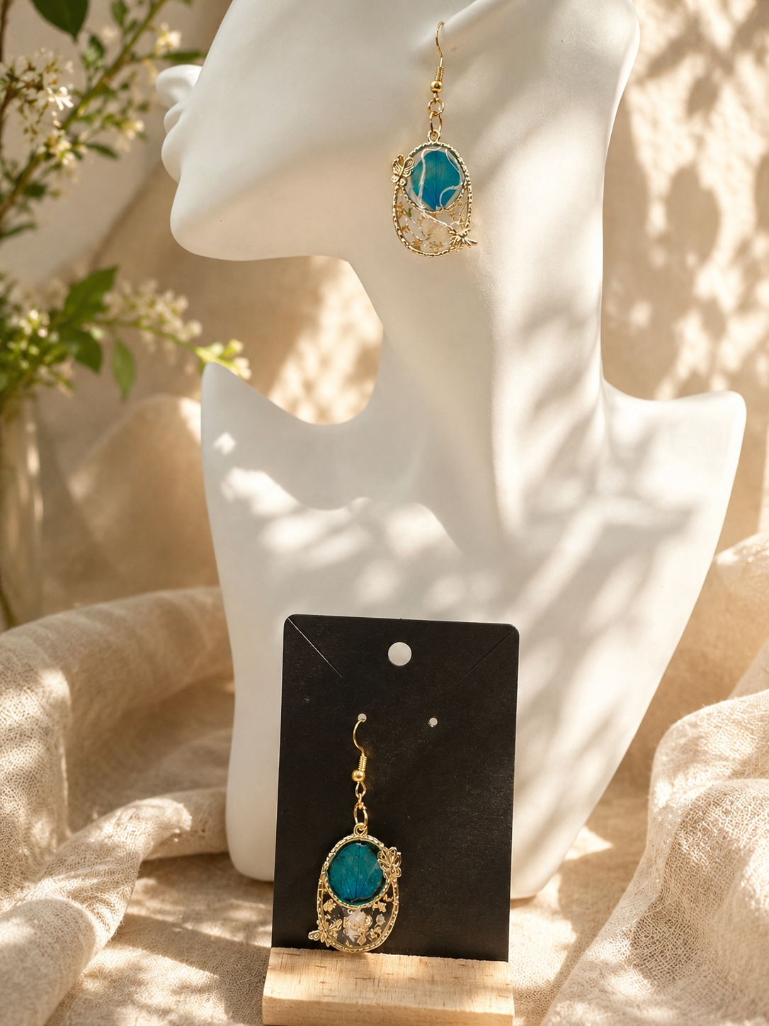 Blue botanical resin drop earring in ornate gold filigree cage frame, displayed on sculptural white bust — handmade by Held Forever Studio