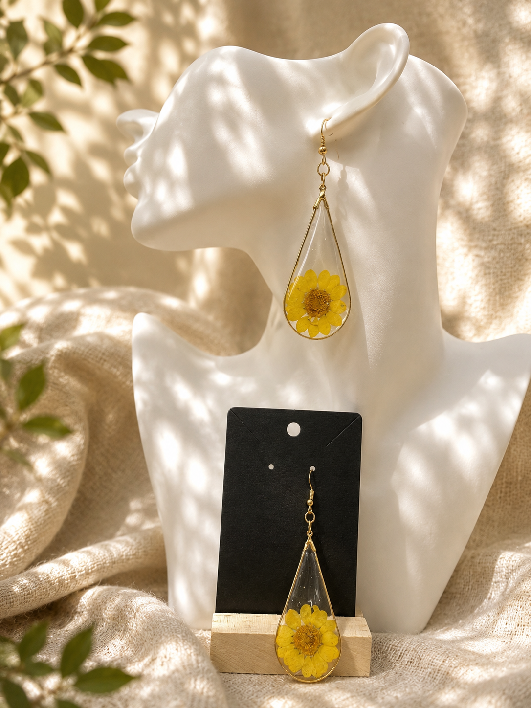 Yellow pressed flower resin teardrop earrings with gold-tone wire frame, displayed on jewellery stand, handmade by Held Forever Studio in Lancashire UK