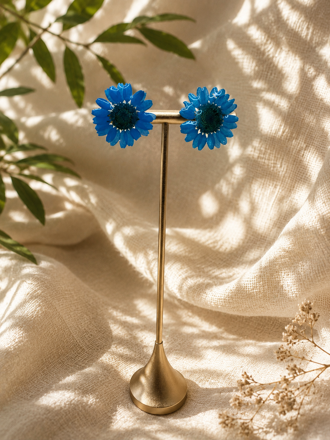 Blue daisy resin stud earrings with 24k gold-plated studs, close up on display stand, handmade by Held Forever Studio