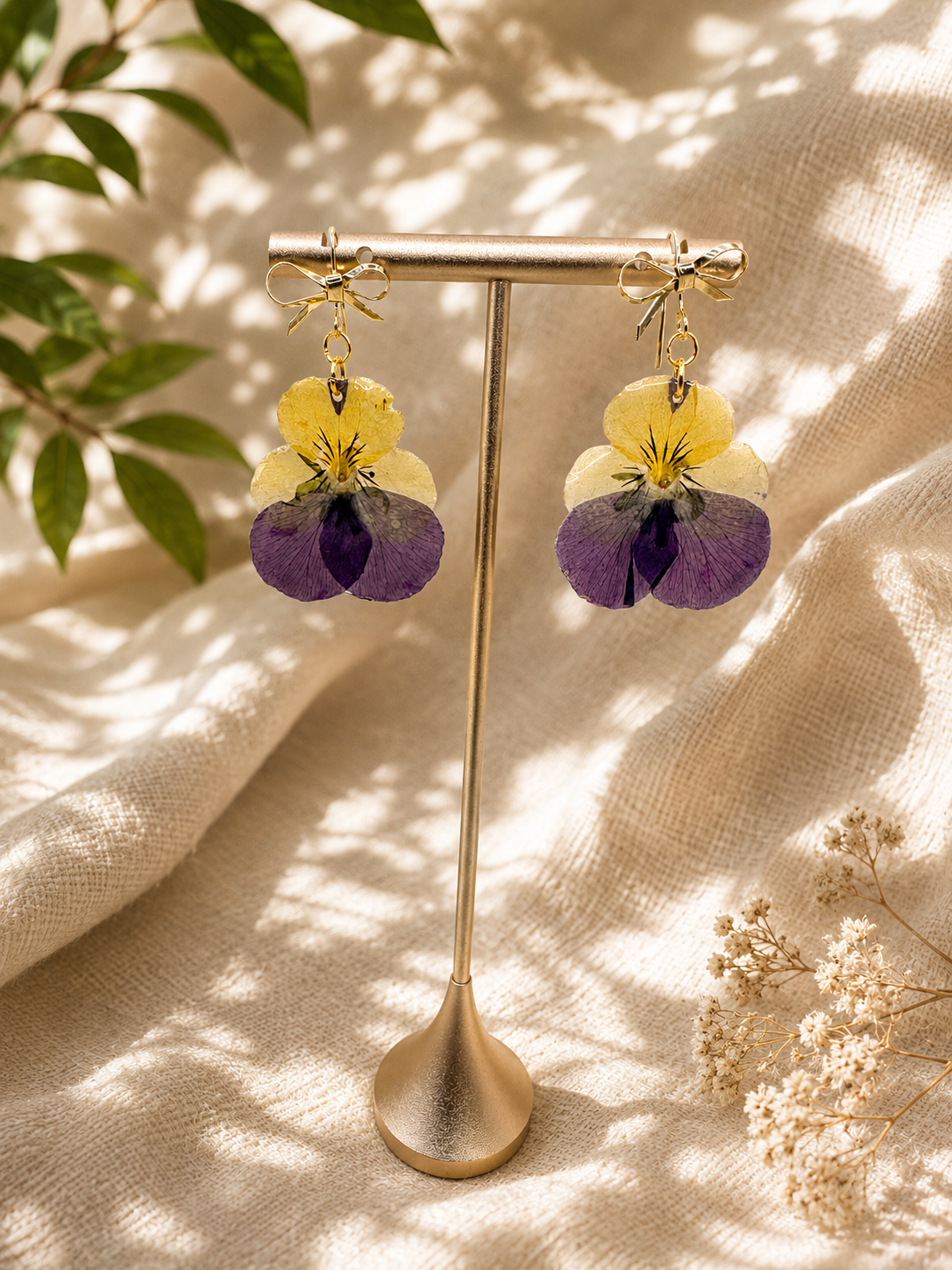Real pansy resin drop earrings with 14k gold-plated bow hook on display stand, handmade by Held Forever Studio