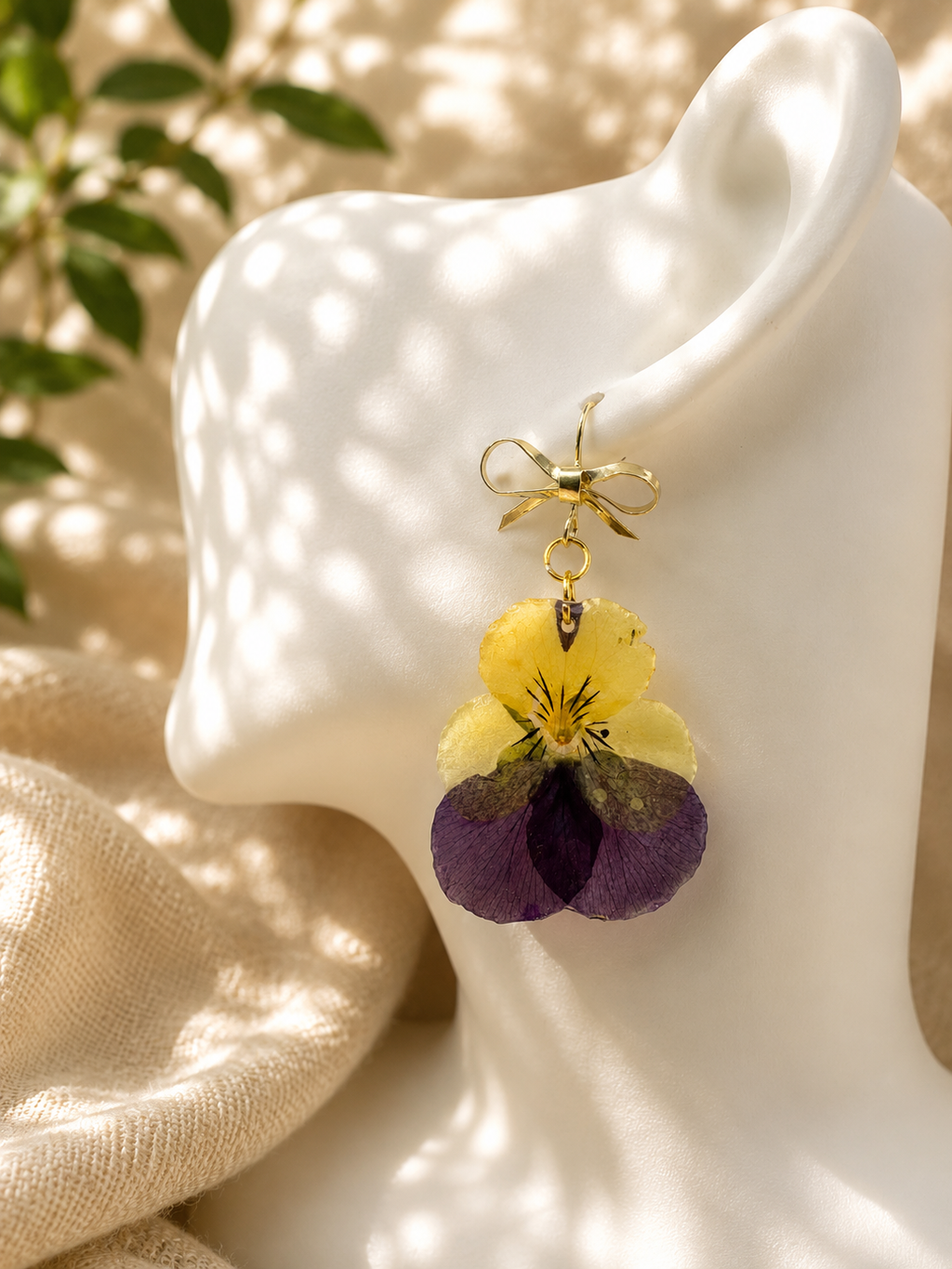 Close up of real pansy resin drop earring with gold bow hook on ear, handmade in Lancashire UK