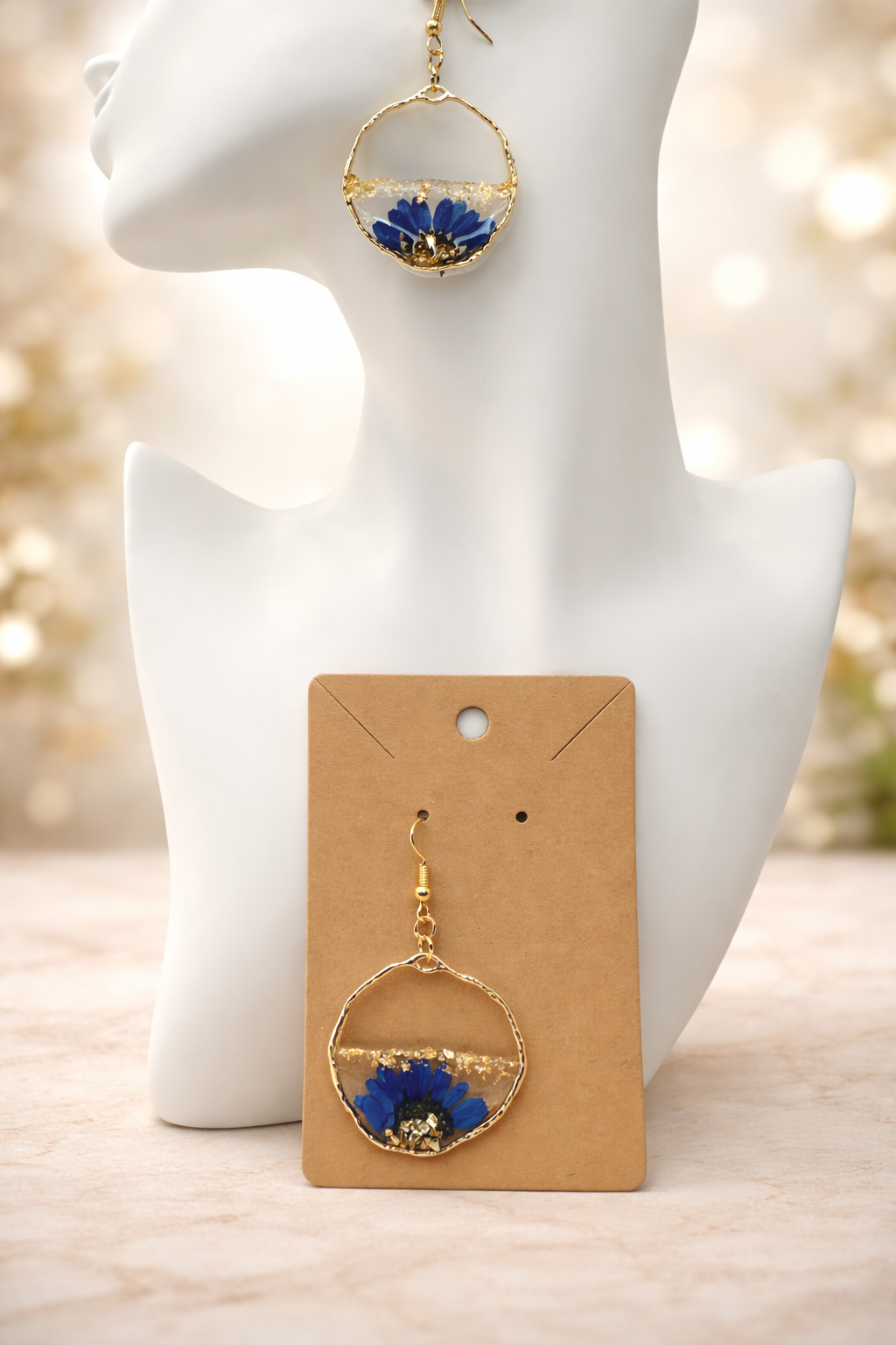 Pair of pressed blue cornflower resin drop earrings with gold leaf displayed on earring card, handmade in Lancashire UK by Held Forever Studio