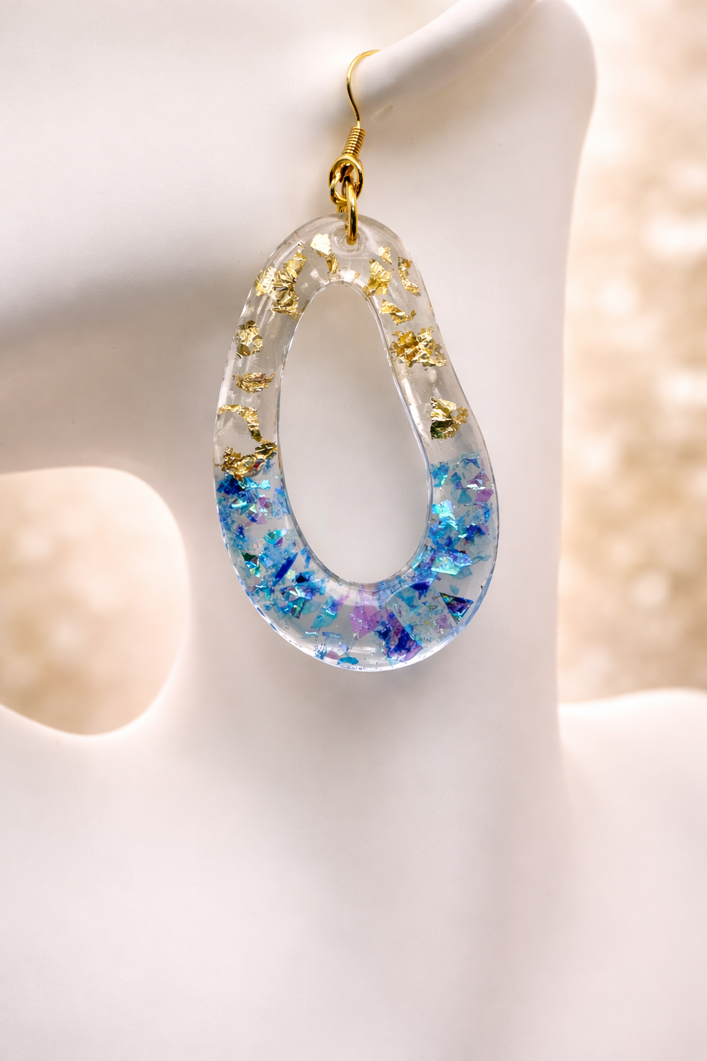 Close up of blue iridescent resin teardrop earring with gold leaf detail, handmade in Lancashire UK
