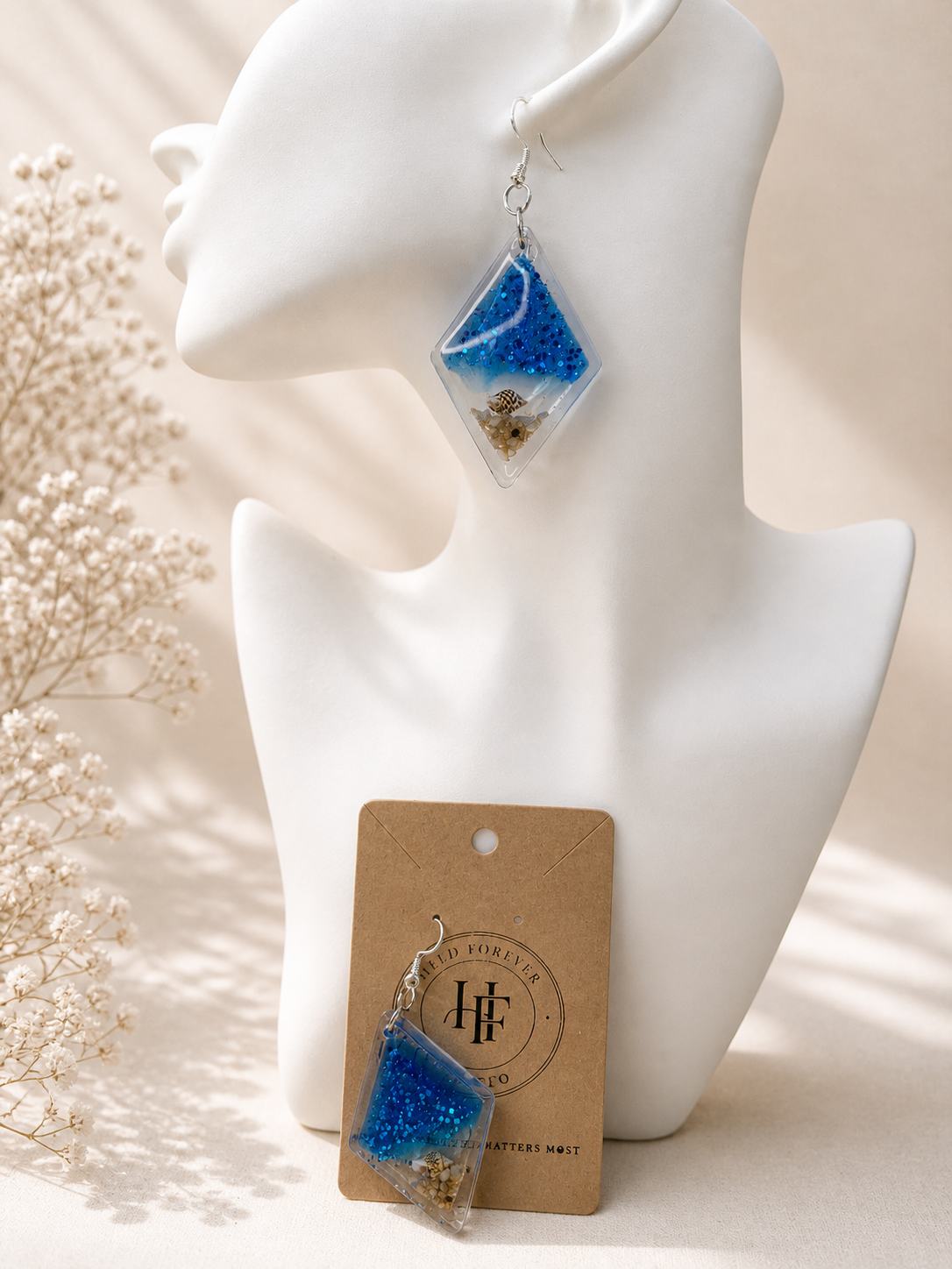 Close-up of ocean diamond resin drop earring showing blue glitter, white wave layer and real seashell detail, handmade in Lancashire UK