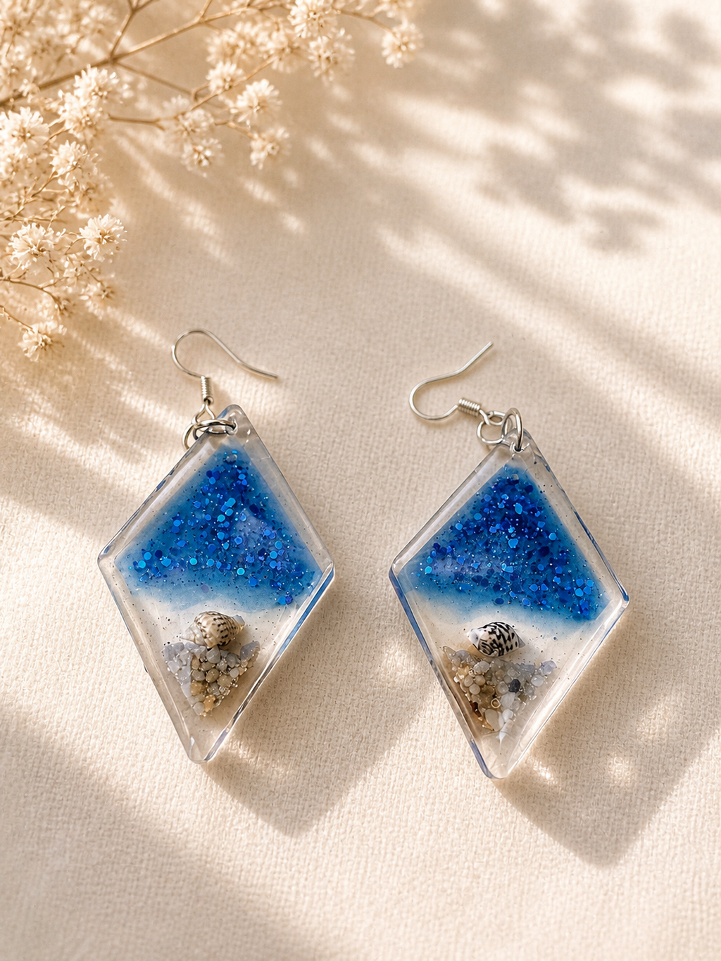 Ocean diamond resin drop earrings on arch display stand, blue glitter ocean scene with real seashell and sand, handmade by Held Forever Studio Lancashire UK