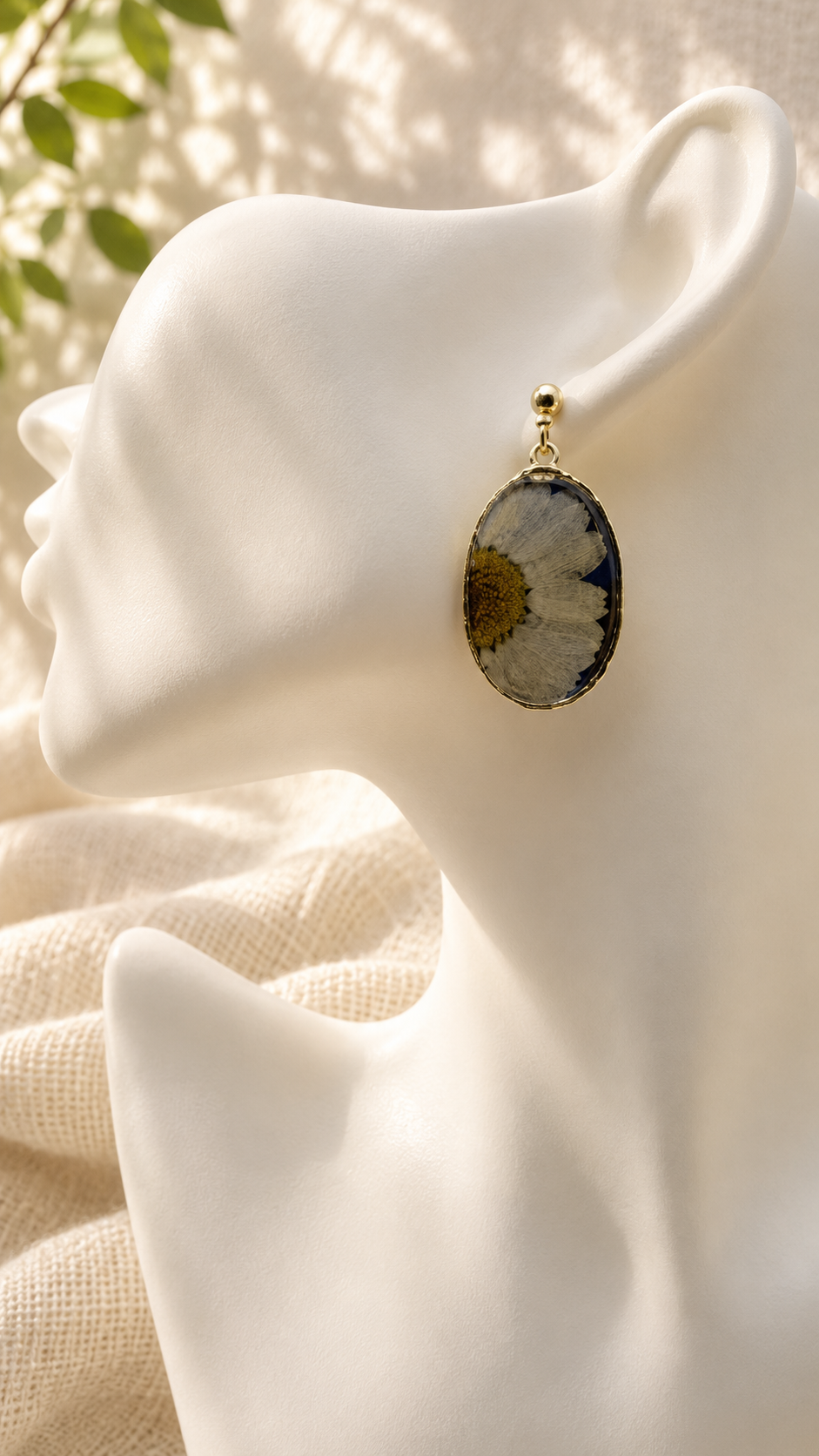Close up of pressed daisy resin oval drop earring worn on the ear, real daisy set in navy resin, handmade in Lancashire UK