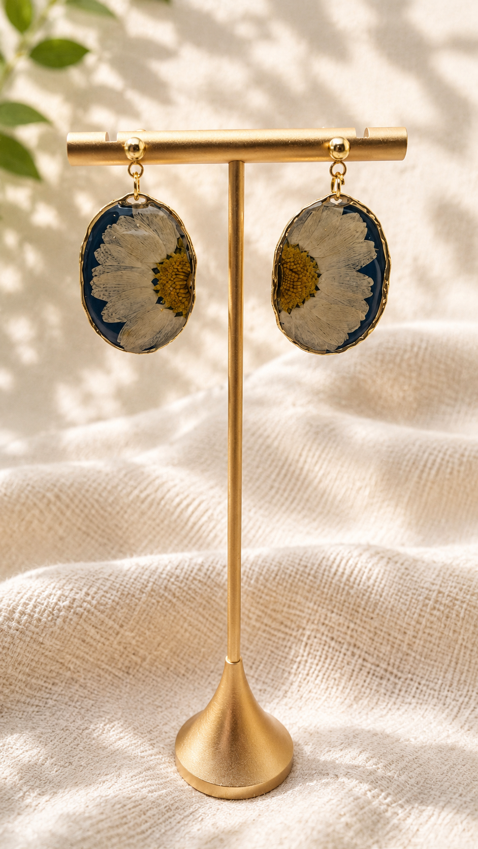 Pair of pressed daisy resin oval drop earrings on a gold stand, navy resin background with 24k gold-plated stud tops, handmade by Held Forever Studio