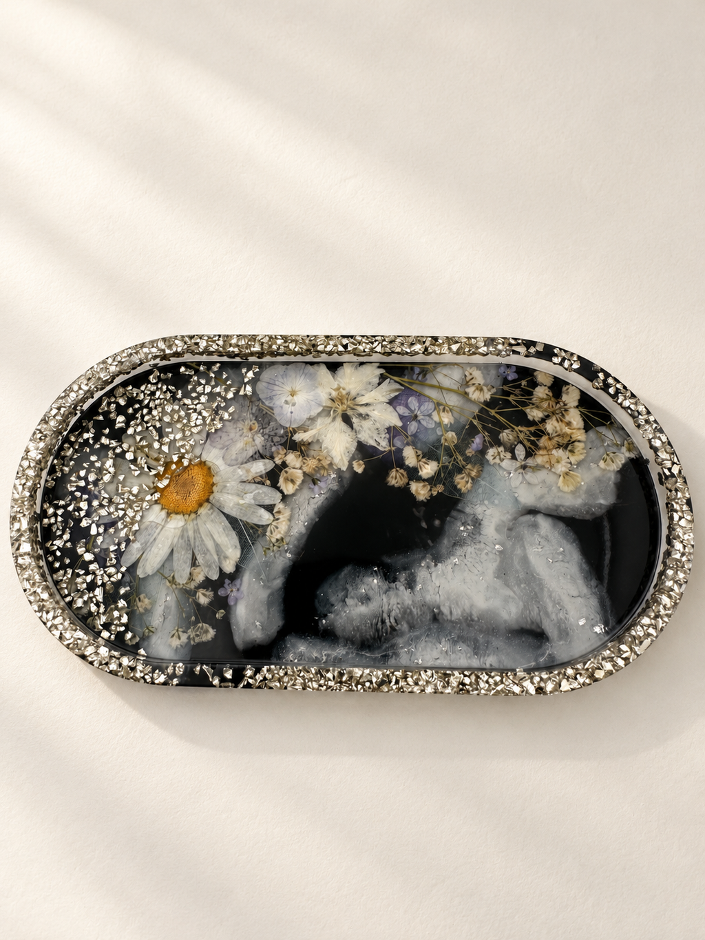 Top view of an oval resin jewellery tray with real pressed flowers, charcoal marbling and silver-coloured details, handmade in Lancashire UK by Held Forever Studio